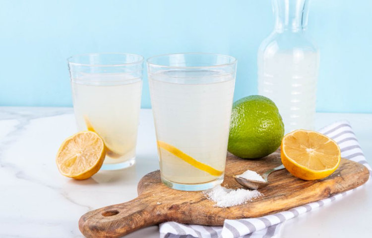 Dva poháre s domácim elektrolytovým nápojom z citróna a limetky so soľou na drevenej doske, zobrazujúce prirodzenú prípravu najlepších elektrolytov na hydratáciu.