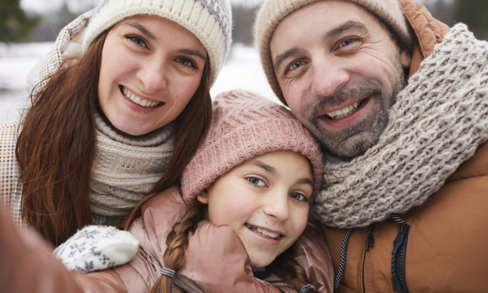  Usmiata rodina v zimnom oblečení sedí na zasneženom svahu so lyžami v pozadí, čo symbolizuje silnú imunitu počas chrípkovej sezóny a význam stopových prvkov ako zinok a selén pre obranyschopnosť organizmu.