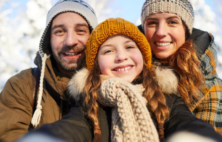 Rodičia s dcérou v čiapkach a šáloch si robia spoločnú zimnú fotografiu na snehu, čo poukazuje na podporu imunity počas chrípkovej sezóny a dôležitú rolu stopových prvkov v prevencii ochorení.