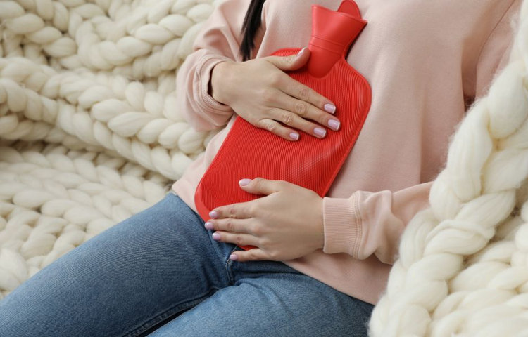 Žena drží červený termofor na bruchu, používa ho na zmiernenie bolesti alebo kŕčov