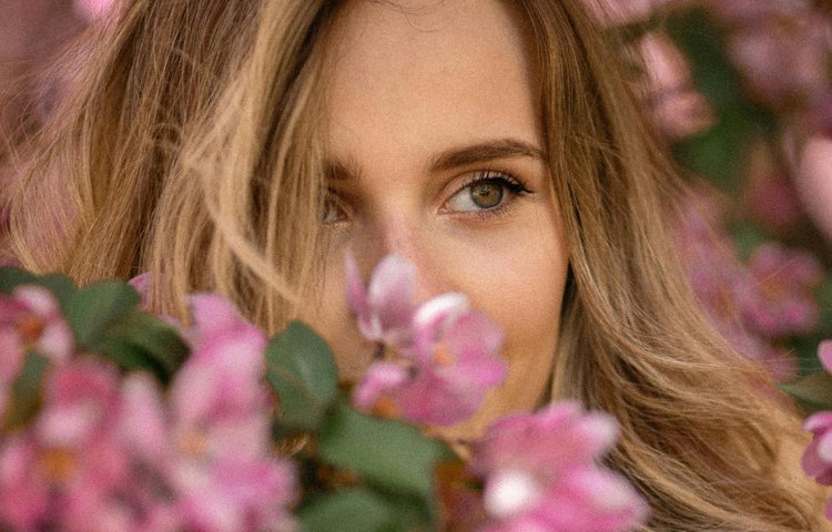 Portrét ženy medzi kvitnúcimi kvetmi znázorňuje sviežu, zdravú pleť na jar, regeneráciu pokožky a prirodzený jas po zimnom období.