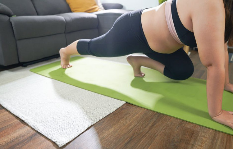 Žena cvičí doma na podložke v obývačke, čo znázorňuje novoročné predsavzatie pravidelne sa hýbať, budovať kondíciu a vytrvať v cvičení aj bez návštevy posilňovne.