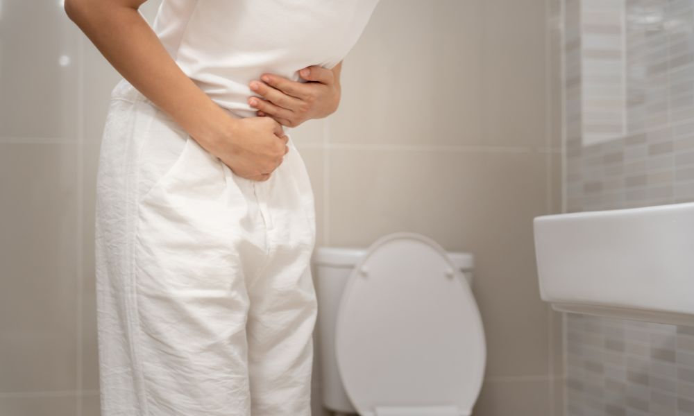  Tehotná žena si drží podbruško v kúpeľni, čo poukazuje na zápchu v tehotenstve spôsobenú hormonálnymi zmenami, tlakom maternice a potrebou šetrnej liečby zápchy.