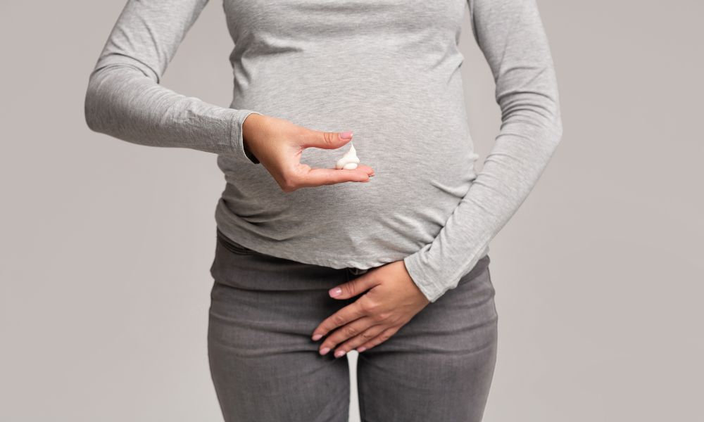  Tehotná žena drží v jednej ruke tubu s krémom a druhou rukou si prikrýva oblasť panvy, čo symbolizuje liečbu kvasinkovej infekcie v pošve počas tehotenstva. Kvasinková infekcia sa môže objaviť aj v tomto období